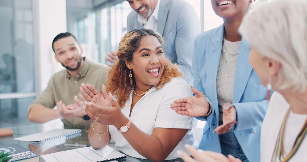 A diverse group of interns and professionals is applauding and celebrating a success in a corporate meeting