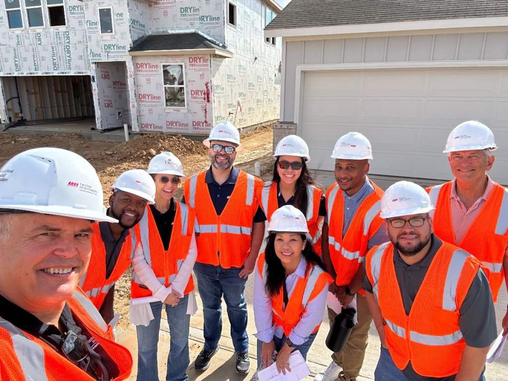 picture of the team wearing hard hats and safety vests in front of a home under construction