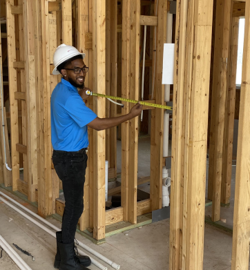 man standing inside a home under construction measuring an opening