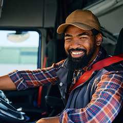A happy truck driver is smiling from the cab of his blue semi-truck.