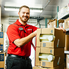 A smiling Pilot Flying J team member is proudly standing next to boxes in a stockroom.