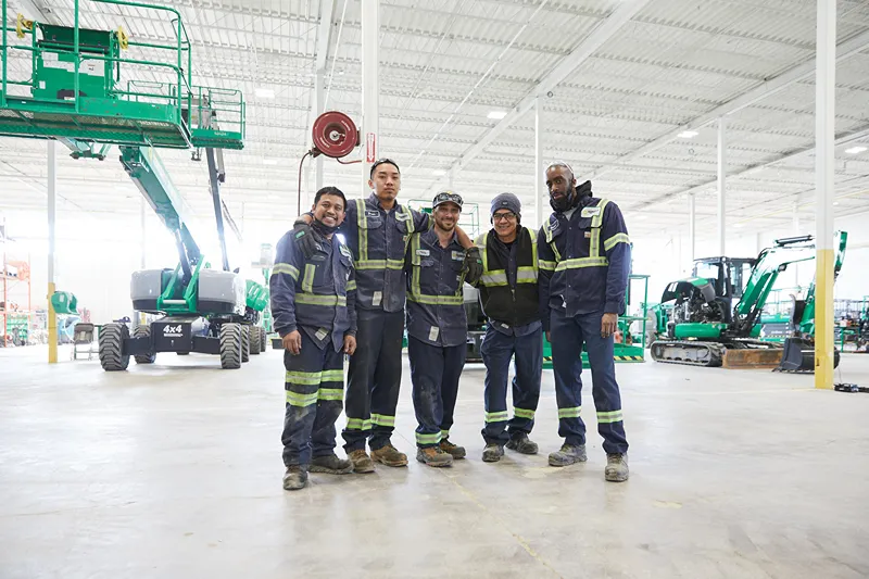 A diverse group of individuals poses together in front of Sunbelt Rentals' logo, showcasing unity and camaraderie.