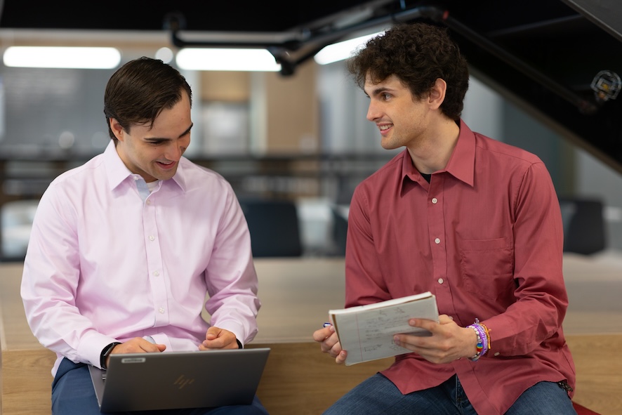 2 men sitting with a laptop and notebook
