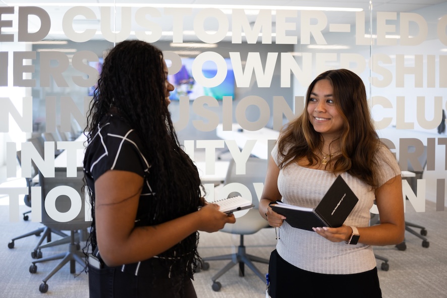 2 women smiling at each other while holding notebooks
