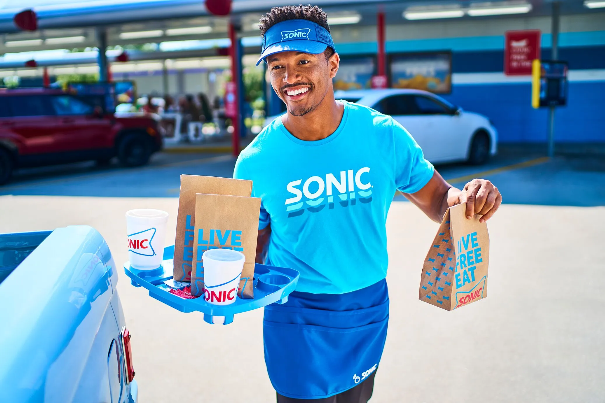 Employee delivering a tray with Sonic food and drinks to a car.