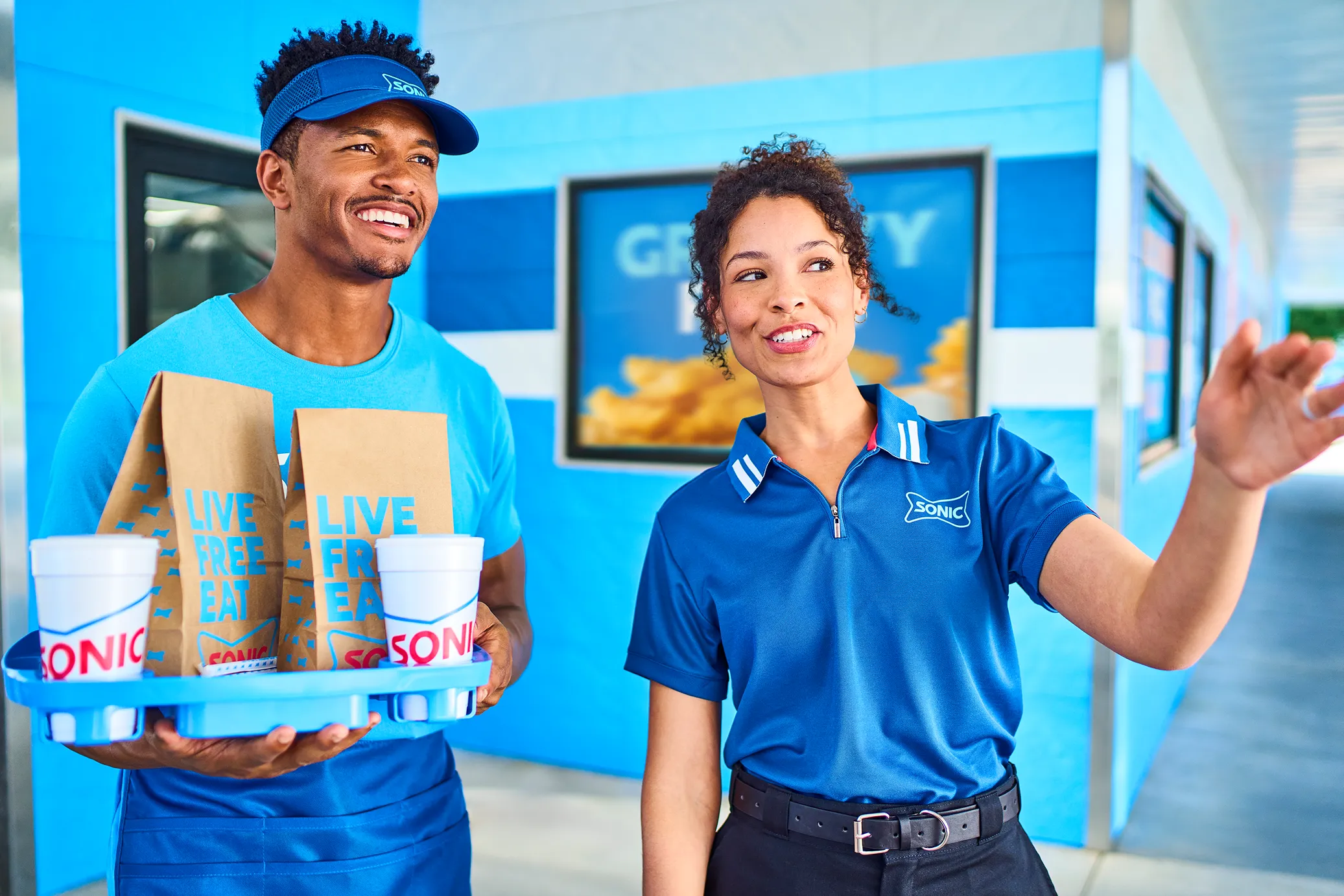 Sonic carhop petting a dog in a car while holding an order.