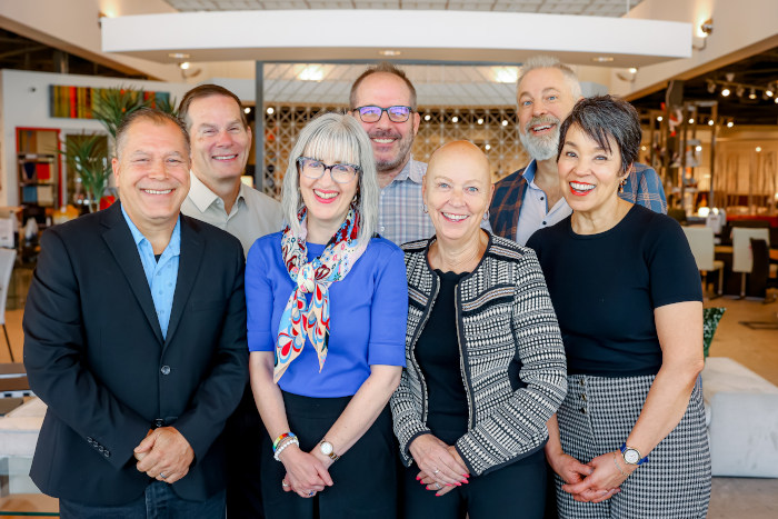 A diverse group of individuals standing together in a well-lit room, engaged in conversation and collaboration.