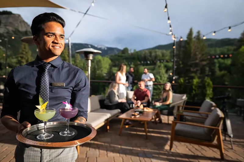 Waiter carrying drinks on tray at outdoor patio with people in background