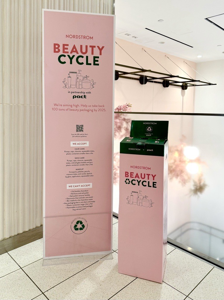 A person depositing a pink bottle into a Nordstrom BEAUTYCYCLE recycling bin