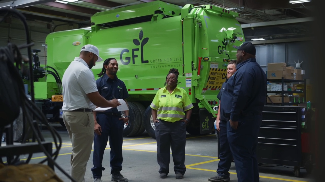 Trois ouvriers de GFL Environmental portant des casques et des lunettes de sécurité examinent des documents à l'extérieur.