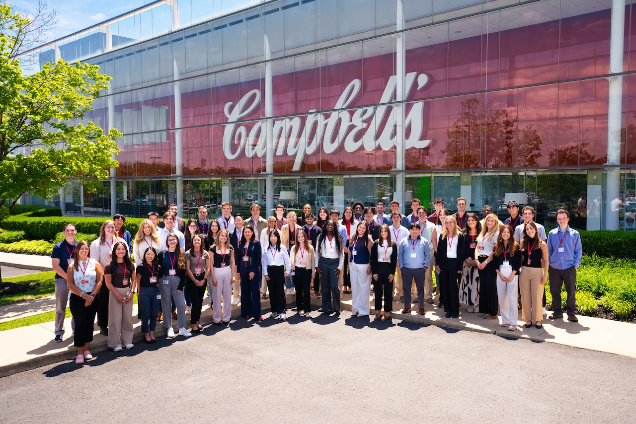 Group of early career employees pose for a photo in front of a company wall