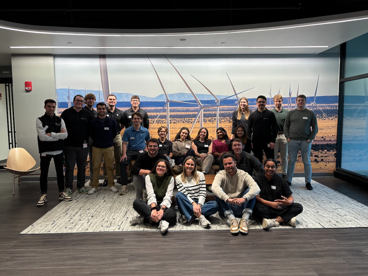 A group of people pose for a photo with an image of several wind turbines in the back
