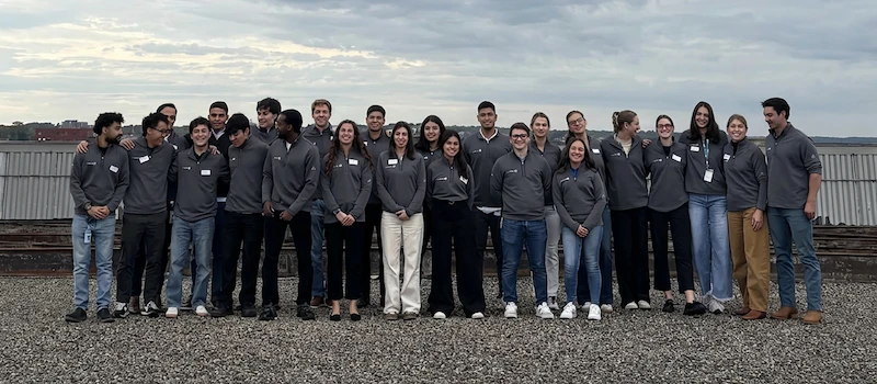A group of people pose for a photo outside with a large metal structure in the background