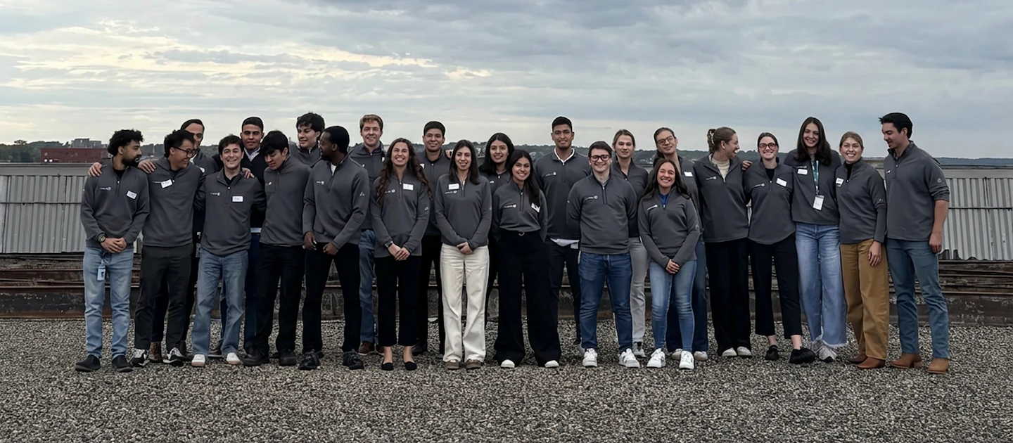 A photo of a large group of people standing outside with a large metal object in the background