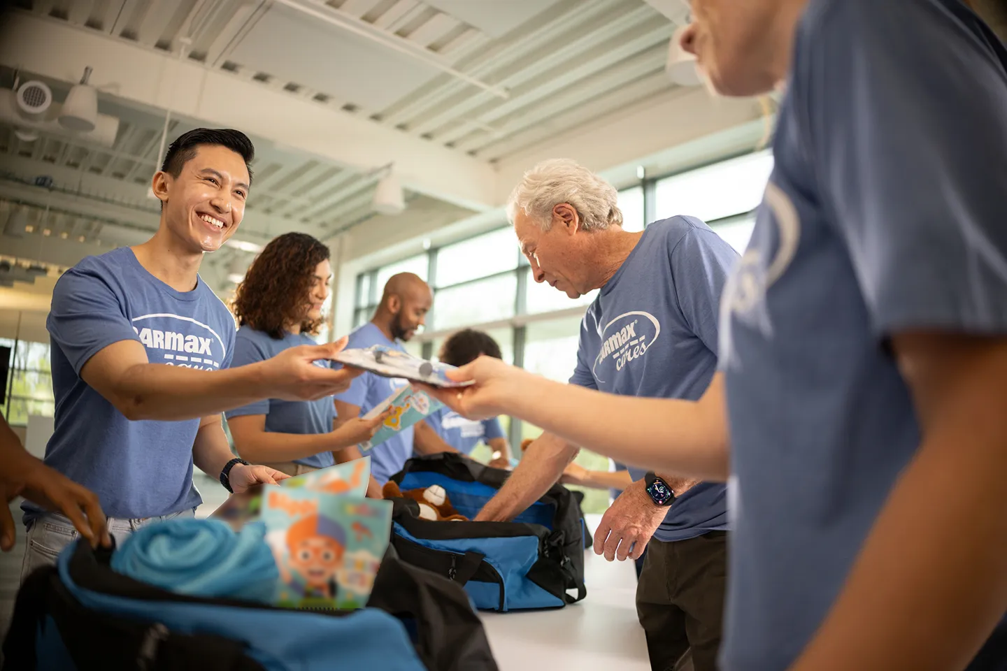 Smiling CarMax employees are volunteering by packing essential items into bags for a community service event.