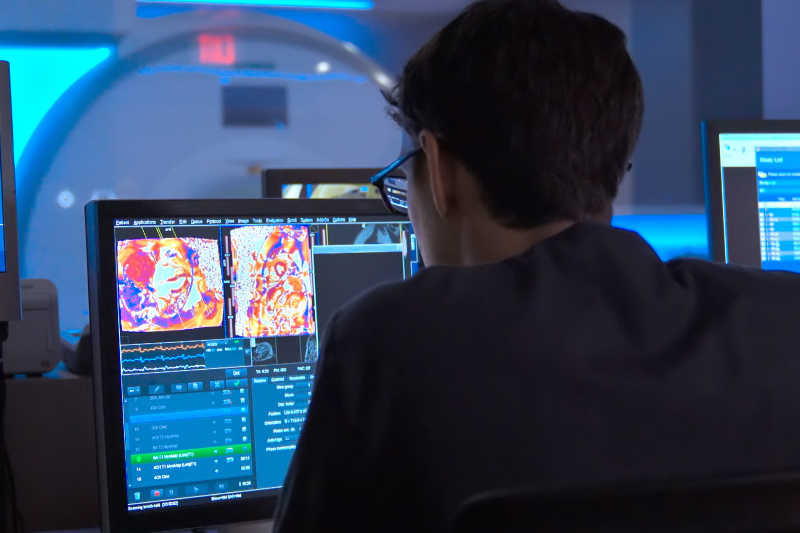 A man wearing glasses looking at the results of an mri scan on a computer