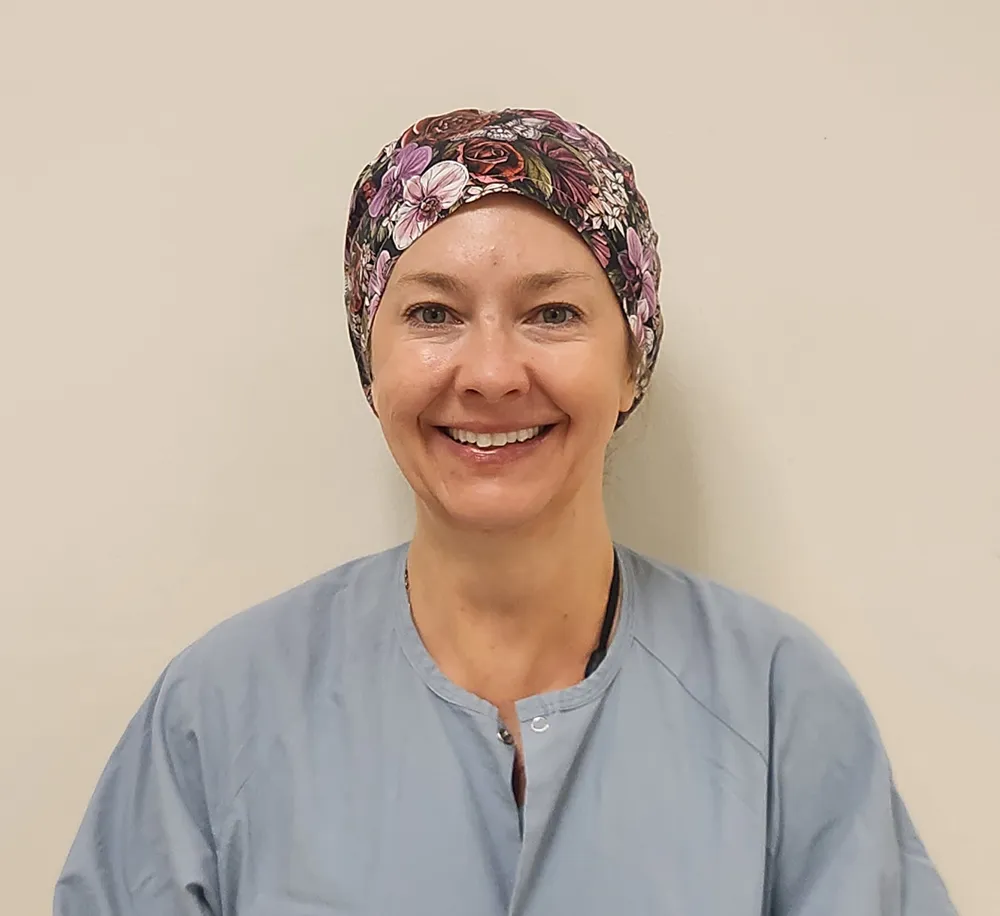 Smiling woman wearing a floral scrub cap and light blue scrubs
