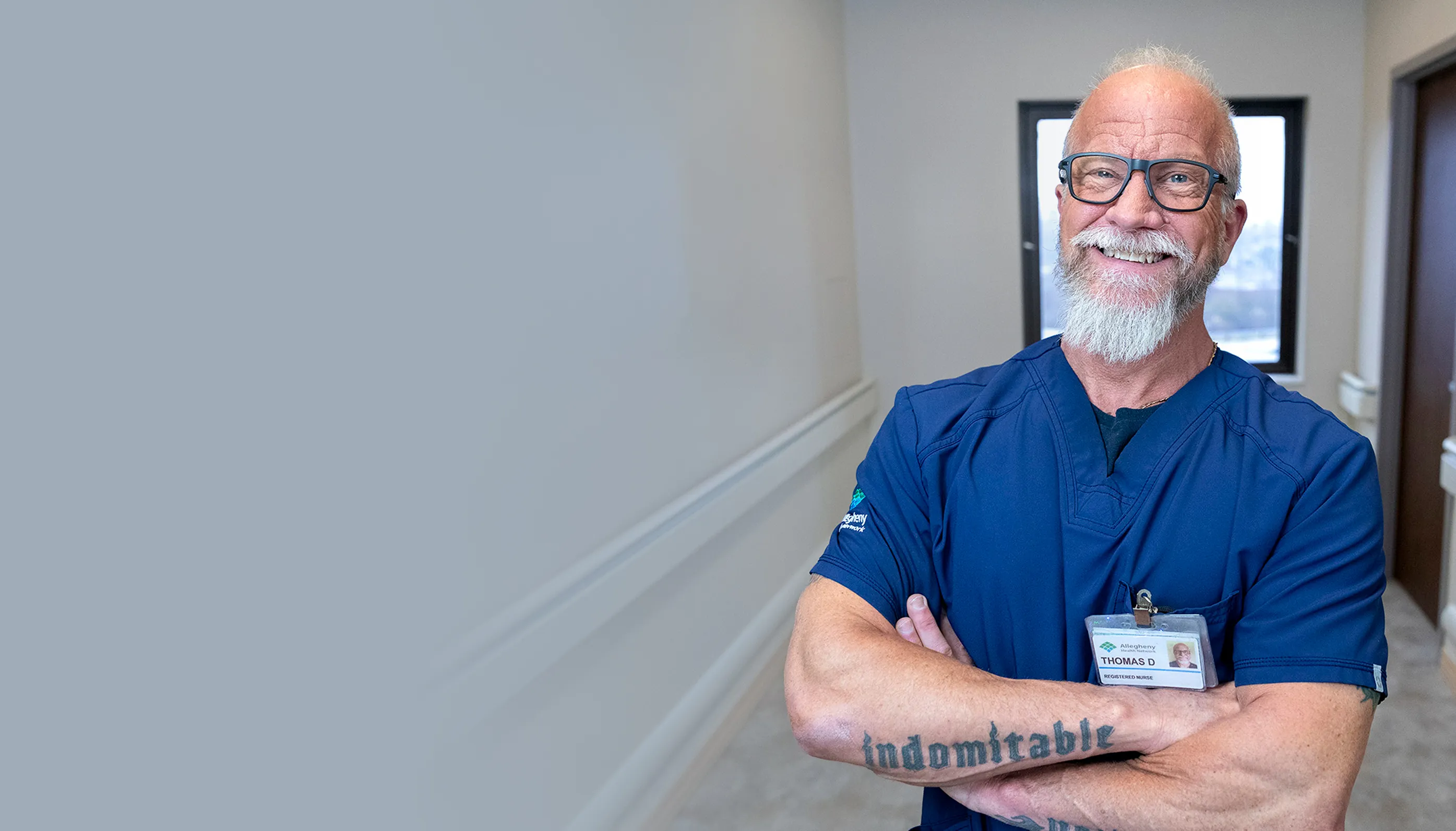 Smiling male nurse in scrubs with arms crossed and ID badge